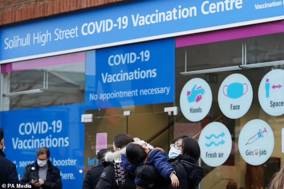 A woman holds a child in a queue at a vaccination centre on Solihull High Street, West Midlands (Jacob King/PA)